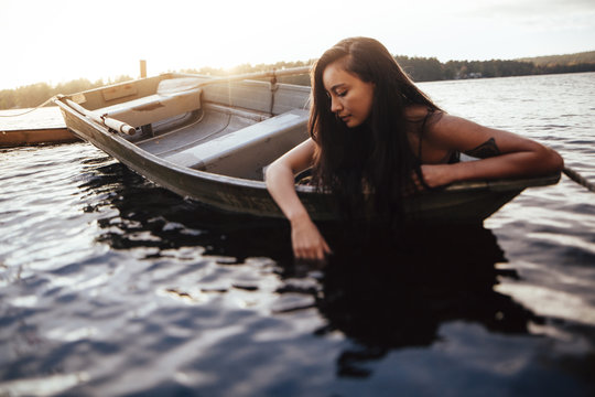 Brunette woman leans into the water on the bow of the boat 