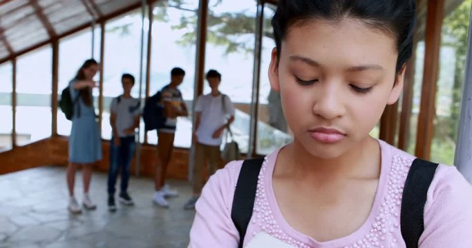 School friends bullying a sad mixed race girl in corridor