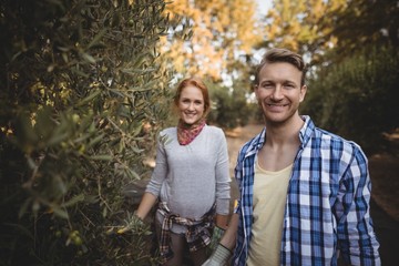 Smiling young couple standing by olive trees at farm