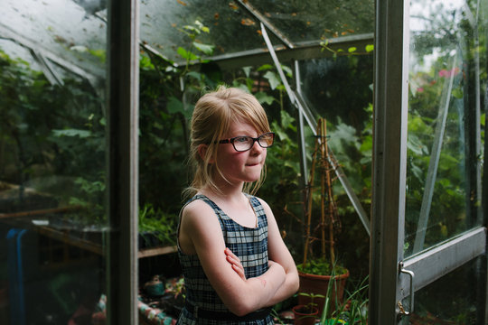 Young girl stands thoughtfully at the entrance to a garden glasshouse