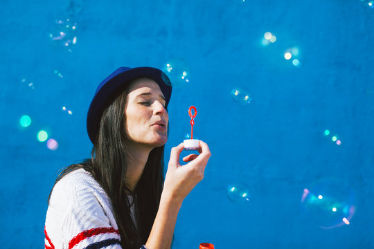 Young woman blowing soap bubbles on blue background 