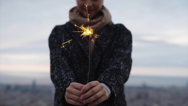 Smiling woman holding a sparkler above city in winter 