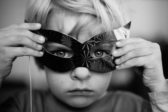 Boy holds paper mask over his eyes
