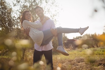 Happy young man carrying girlfriend while standing at olive farm