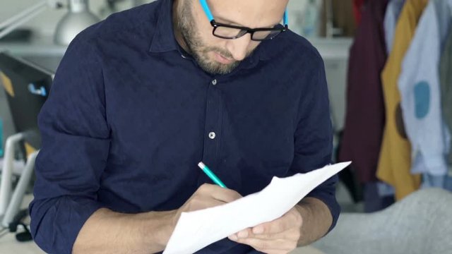 Young man analyzing documents and making notes standing at home
