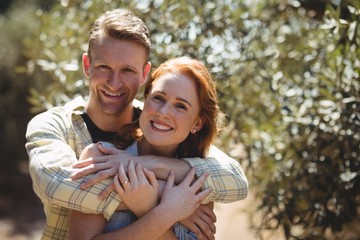 Happy couple embracing by trees at olive farm