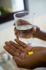 Cropped hands of person holding medicines and drinking water