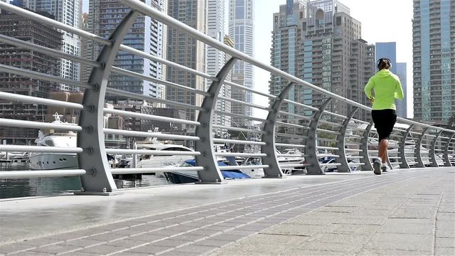 Low angle view of athletic fitness woman running jogging in Dubai Marina in the morning, slow motion