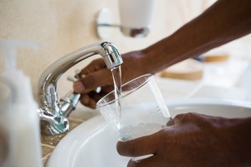 Cropped hands of man filling water in glass at sink - Powered by Adobe