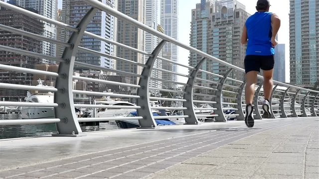 Low angle view of athletic fitness man running jogging in Dubai Marina in the morning, slow motion