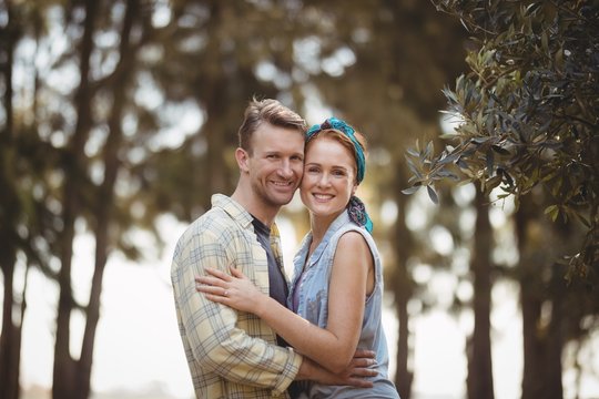 Smiling young couple embracing by olive tree at farm