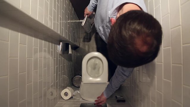 Man flushing the toilet, he presses the button on the wall, the view from the top