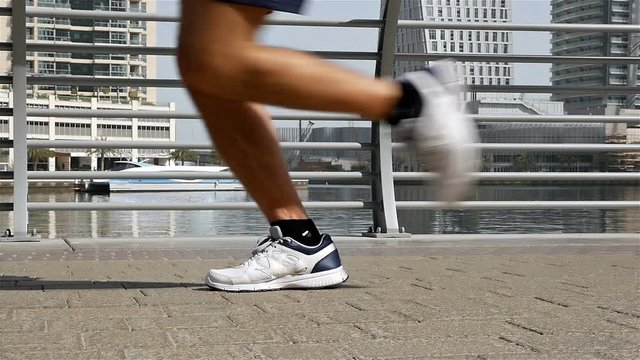 Close up of athletic fitness man legs running jogging in Dubai Marina in the morning, slow motion