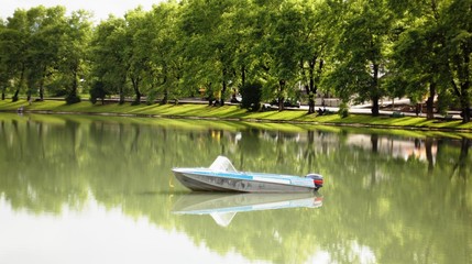 A motor boat on the lake, drifting lonely on the water in the rays of the setting sun against the backdrop of shadows from trees standing on the shore around the lake. A calming landscape .