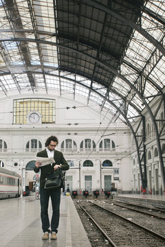Young businessman holding newspaper checking the time waiting on train station