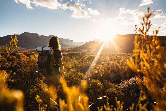 Woman hiking with a backpack through a mountainous valley at sunset