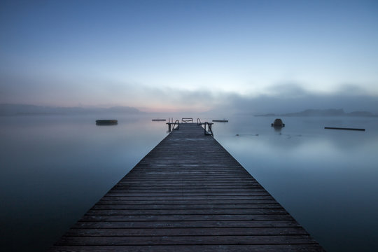 wooden dock on a lake in morning fog at sunrise