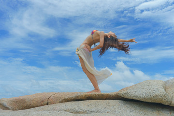 strong woman in bikini enjoy the sea beach by standing on the rock withcurl up the body with blue sky in background