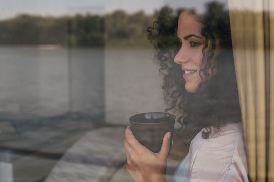 Woman looking through window and holding her tea