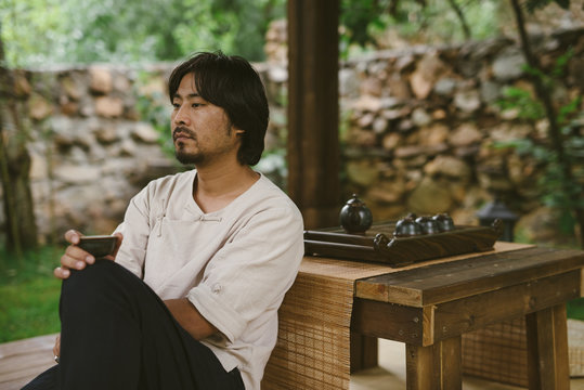 Man in traditional Chinese clothing drinking tea in a garden