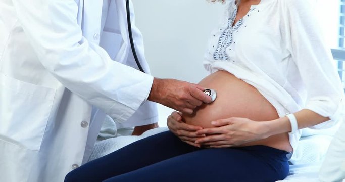Doctor examining pregnant womans belly with stethoscope in ward