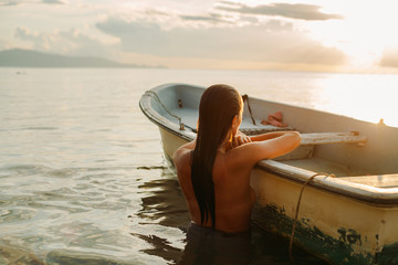 Girl in the sea leaning on a fishing boat