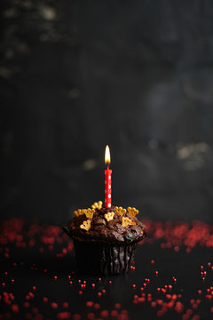 Single candle in a chocolate cupcake with gold crowns
