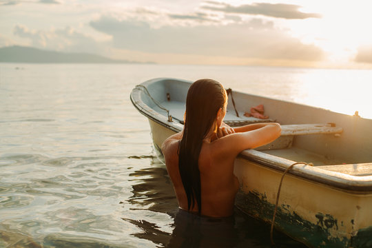 Girl in the sea leaning on a fishing boat