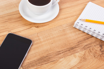 Mobile phone or smartphone with notepad for writing notes and cup of coffee, copy space for text on board