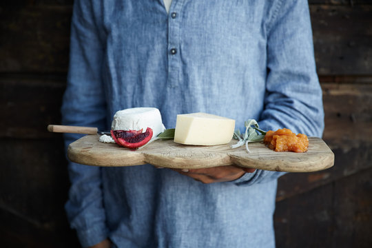 Man holding rustic cheese plate inside a barn