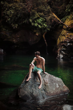 A young man rests on a rock in the middle of a summer swimming hole