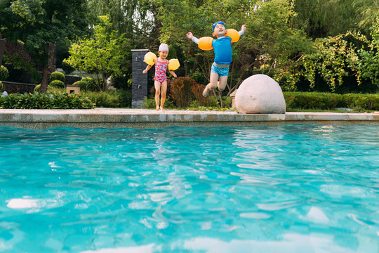 Two kids jumping into swimming pool