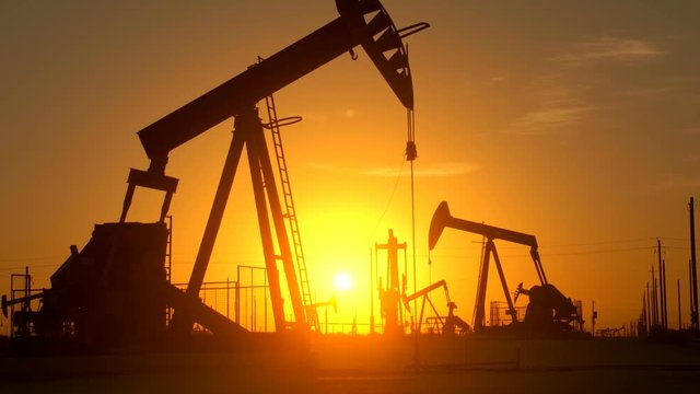 The silhouette of oil pumps in a large oil field at sunrise.