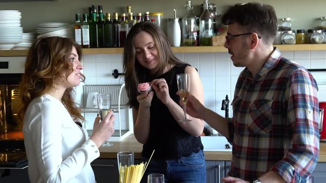 two girls and guy celebrate birthday and clink glasses with champagne and eat cupcakes on the kitchen