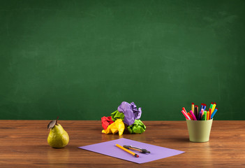School items on desk with empty chalkboard