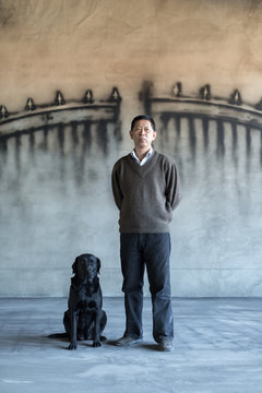 A man and dog in front of a wall with a gate painting on it