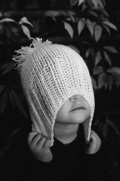 A little girl clasps the woolly hat she is wearing pulling it over her eyes