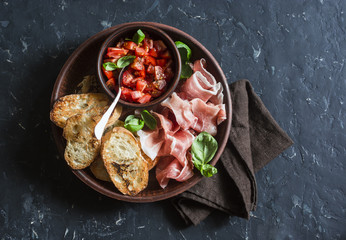 Italian antipasto - tomatoes bruschetta and prosciutto. On a dark background, top view. Delicious snack or appetizer for wine