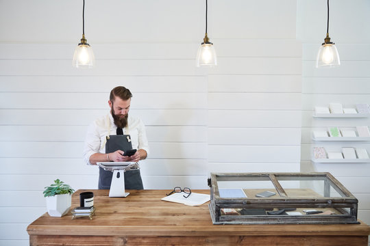 Small Business Owner Texting On Mobile Phone In Artisan Retail Shop