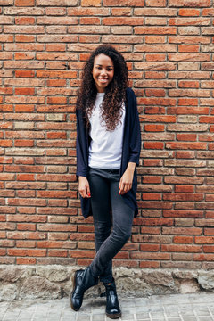 Young african woman smiling in front of a brick wall in the city 