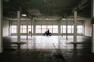 Young man on motor bike in big empty warehouse