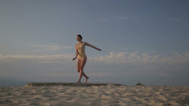 Young beautiful woman is dancing wearing body suit on sunrise in the desert. Creative authentic concept.