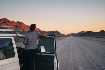 Woman on a road trip through the desert leaning out of her car watching a sunset