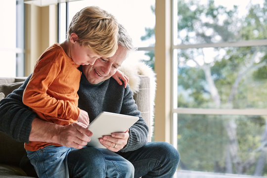 Father and son looking at digital tablet in on sofa in living room