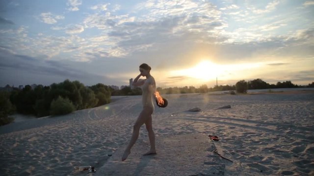 Young beautiful woman is dancing with fire wearing body suit on sunrise in the desert.