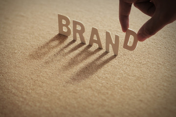 BRAND wood word on compressed or corkboard with human's finger at D letter.