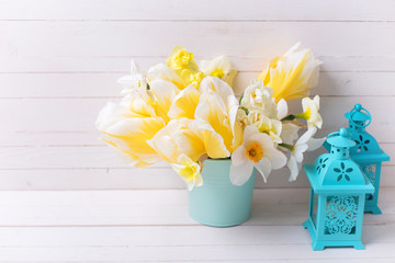 Bright yellow daffodils and tulips flowers and lanterns  on white wooden background.