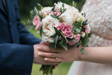 Beautiful wedding bouquet of white and pink peony in bride's and groom's hands in blur