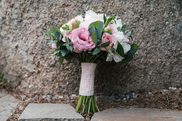 Beautiful wedding bouquet of white and pink peony and roses in natural stone in blur outdoors, close up