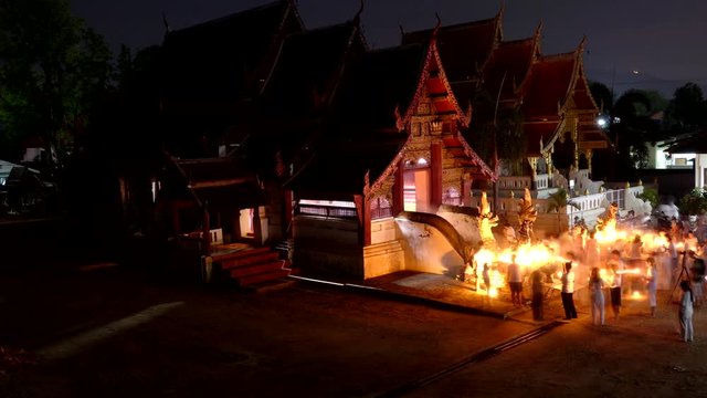  People and monk walk with lighted candle in hand around  wat in  time lapse